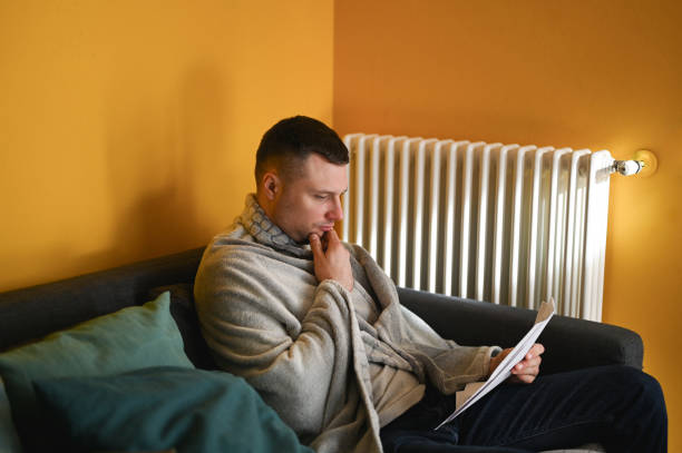 istock Serious man wrapped in blanket sitting on sofa. home energy consumption. 1794641369