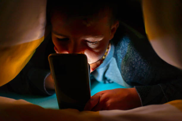 istock Serious boy,face under the blanket at night in his bed communicates on Internet.Child gadget addiction and insomnia.Selective focus. 1794641456