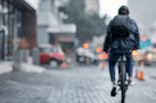 Cyclist, bicycle and delivery in the city on rainy day or cold weather in an urban town on mockup. Biker riding in the rain with cargo, transport or deliver service in a urban town street for courier