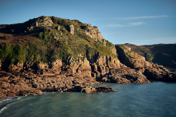 Warm rocky outcrop with green foliage reaching into the aqua blue sea