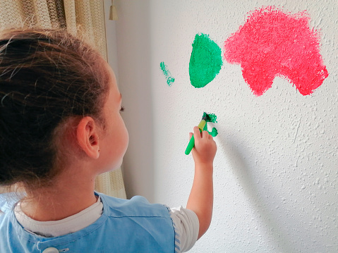 Close-up of a girl engrossed in painting, adding vibrant strokes to the wall. A captivating moment capturing the innocence and creative spirit of childhood.