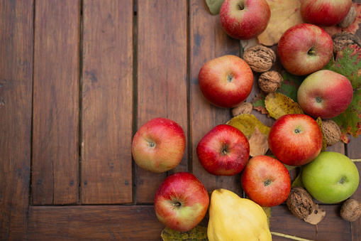 Ripe apples, organic quince, nuts and colorful autumn leaves on wooden table shot from above