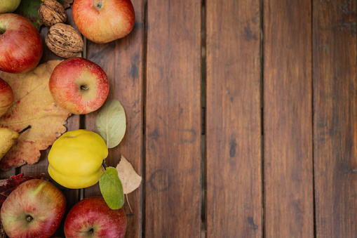 Ripe apples, organic quince, pear, nuts and colorful autumn leaves on wooden table shot from above