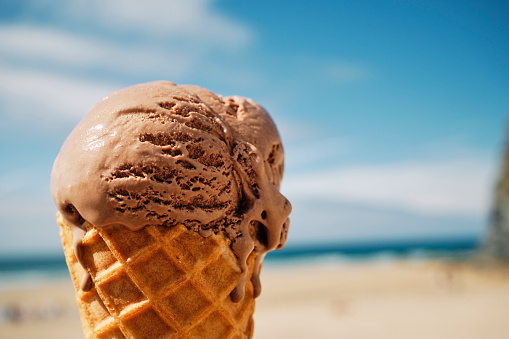 Delicious Chocolate Ice Cream cone at a sunny beach with defocused blue sky and sea, Newquay, Cornwall.