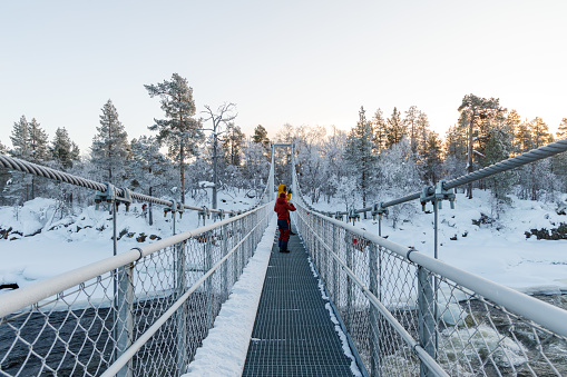 Mother and daughter walking on the bridge over the snowy river
