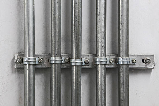 Electrical Metal Conduit Pipes An architectural fixation detail from a surface-mounted electrical metal conduit pipe system isolated on a white wall. canal stock pictures, royalty-free photos & images