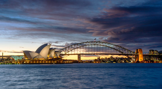Sydney, Australia - August 19, 2018: Evening descends upon Sydney, and the twin icons of Sydney Harbour, the Opera House and the Harbour Bridge, stand out against a dramatic sky.
