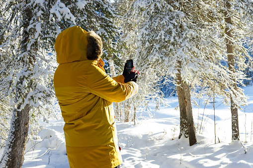 Woman in yellow winter jacket taking a photo with her smart phone