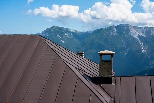 brown sheet metal alpine shelter roof with chimney pot and mountain peaks in the background at dawn on a sunny day