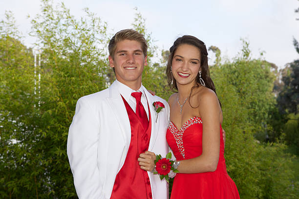 Prom Couple Smiling An attractive prom couple wearing a red dress and white tuxedo smiling outdoors prom stock pictures, royalty-free photos & images