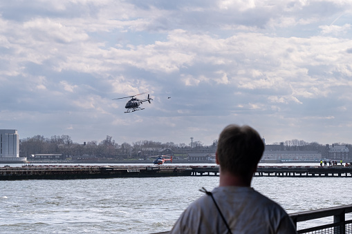 A man watches the mesmerizing sight of a helicopter landing in New York. This image portrays the allure of urban aviation, blending the excitement of flight with the iconic backdrop of the city that never sleeps.
