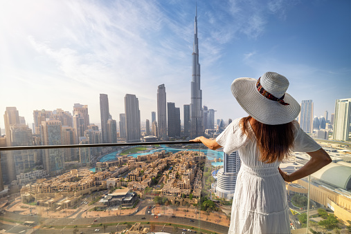 A elegant woman in a white dress looks at the panoramic view of the downtown Business Bay district skyline of Dubai, UAE
