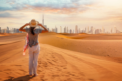 A tourist woman stands in the Red Desert and looks at the distant skyline of Dubai city, United Arab Emirates