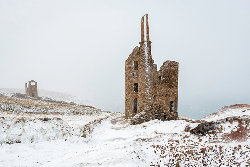 Historic Cornish granite mine buidling engine house on cliff top in snow