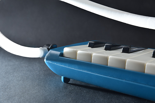 Detail of blue melodica prepared to play on the table with blow tube on black isolated table. Front elevated view.