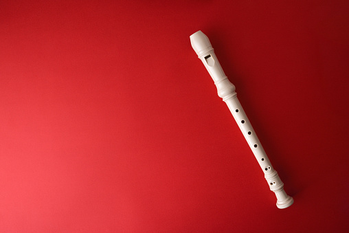 White plastic recorder placed whole diagonally on red gradient background. Top view.