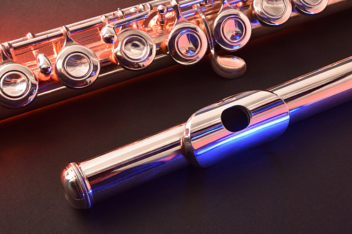 Detail of metal flute head and body on black table with red and blue lights. Elevated view.