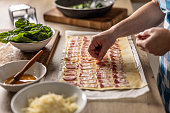 The cook prepares mini pizza cakes, puts pieces of bacon on puff pastry.