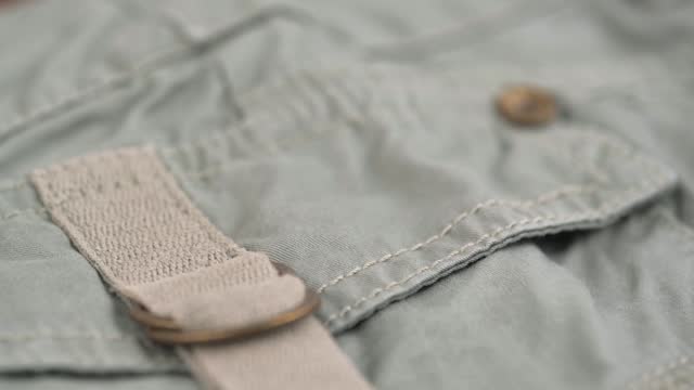 closeup rotation, two metal half-rings on canvas belt of khaki trousers pocket.