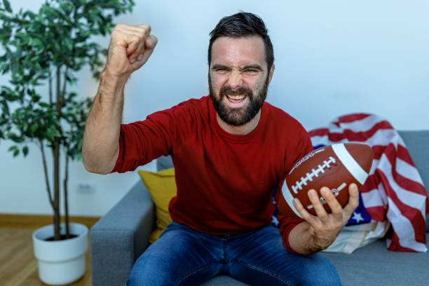 ein junger mann genießt zu hause ein fußballspiel. - sitting 20s adult american football stock-fotos und bilder