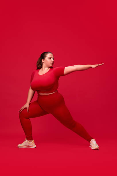 istock Plus size model. Young woman with fat, overweigh body training, doing exercises against red studio background. Sport, body-positivity 1794906285
