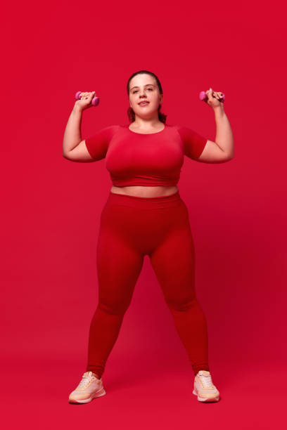 istock Overweight young beautiful woman training, doing exercises with dumbbells against red studio background. Sport, body-positivity 1794906292