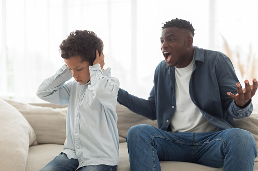 Child Abuse Problem. Angry Black Father Shouting At Scared Little Son, While Unhappy Kid Boy Covering Ears At Home. Family Issues And Domestic Violence, Aggressive Dad Concept. Selective Focus