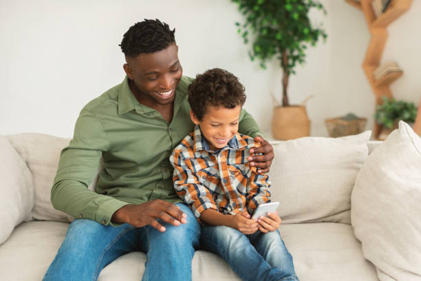 istock Little Boy And His Black Dad Using Cellphone At Home 1794916264