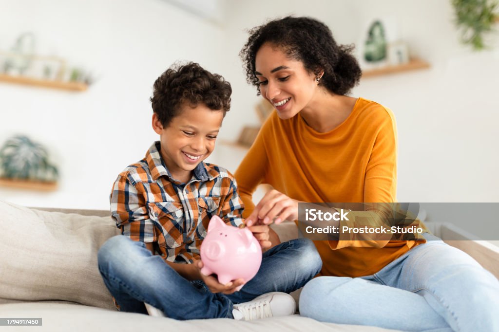 幸せなお母さんと小さな息子が貯金箱屋内にコインを入れる - 貯金のロイヤリティフリーストックフォト 幸せなお母さんと小さな息子が貯金箱屋内にコインを入れる - 貯金のロイヤリティフリーストックフォト