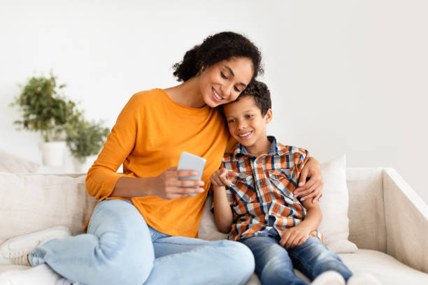 istock Happy Mom And Son Using Smartphone Hugging On Sofa Indoor 1794917710
