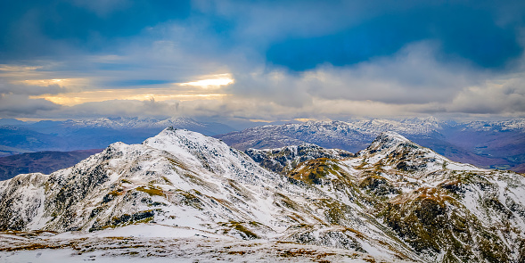 Panoramic view over the snowy mountains of the Highlands in Scotland during an overcast day in winter. Picture taken from Meall Corranaich munro.