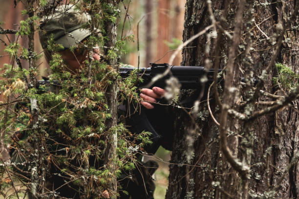 istock Soldier man shooting from weapon from behind tree, dressed in military camouflage uniform, in forest nature. Military male guard in country border holding weapon on war, outdoors. Copy ad text space 1794919200