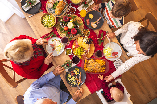 High angle view of happy multi-generation family gathered around the table, having Christmas dinner all together at home, speaking to each other and laughing