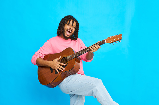 A young man playing the guitar and singing against a blue background