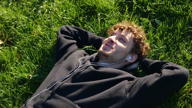 Happy guy lying on the grass in the park and listening to music in headphones. Top view. Lifestyle. Concept of autumn walks. Real time concept.