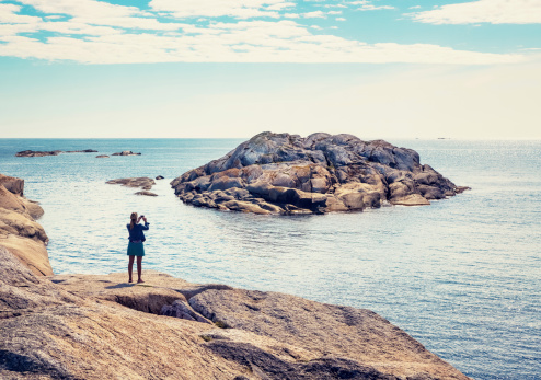 Slope of naked rock with a woman photographing the view with a camera phone at the view at Verdens Ende, Tjøme Vestfold, Norway