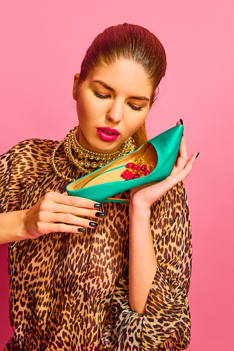 Portrait of lady dressed animal print blouse holding heel full of capsules, vitamins, pills, medications over pink background. Concept of medicine, viruses, immune system, selfcare, healthcare.