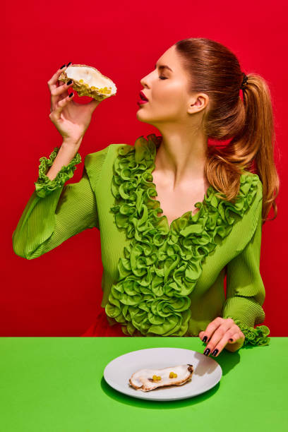 istock One attractive lady sitting at table and eating delicious vitamins, tablets, pills instead o oysters isolated red background. 1794975881