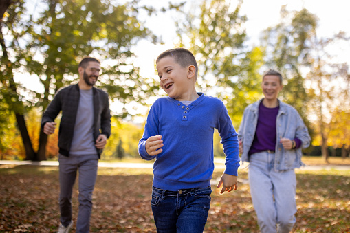 A Caucasian family running together in a public park while having a picnic