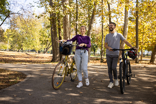A mid adult Man and woman talking while walking their bikes in a public park