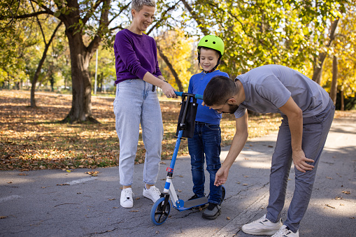 A mid adult Caucasian man helping his son ride a push scooter in a public park