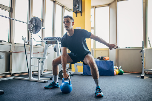 One man, fit young male exercising with kettlebell in gym.