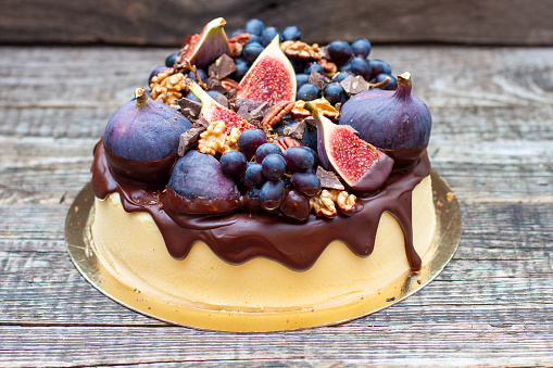 Delicious vanilla cheesecake poured with melted dark chocolate, figs, grape, pecan nuts on the top. Harvest autumn decoration