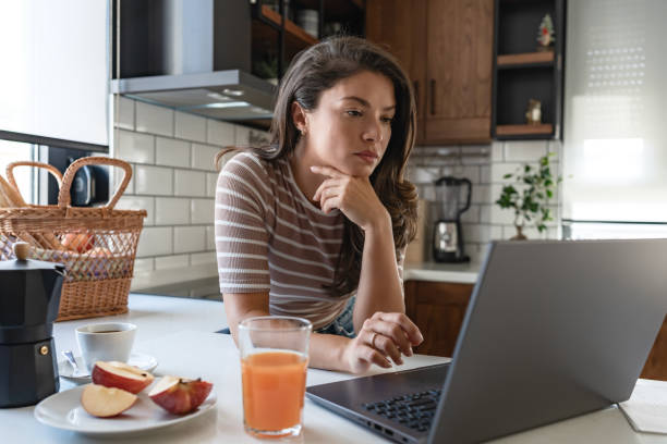 istock Stressed young woman at home, holding financial papers, looking at computer concerned about her finances 1794986201