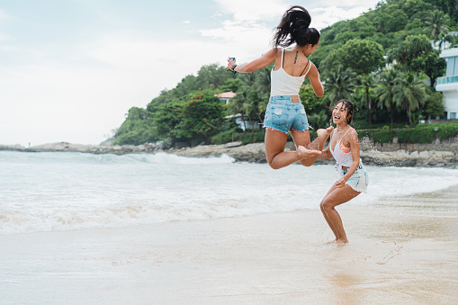 Portrait of happy smiling beautiful women on the beach. Pretty young Asian girl friends holding hands in casual looking clothes laughing in bright sky