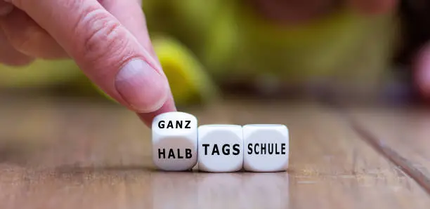 Hand turns dice and changes the German expression 'halbtagsschule' (half day school) to 'ganztagsschule' (all day school).