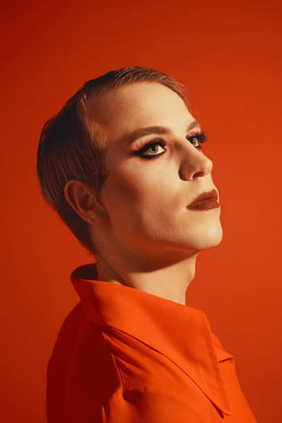 istock Extravagant young man with stylish hairstyle and wright makeup, lipstick and lashes posing against red studio background 1795006329