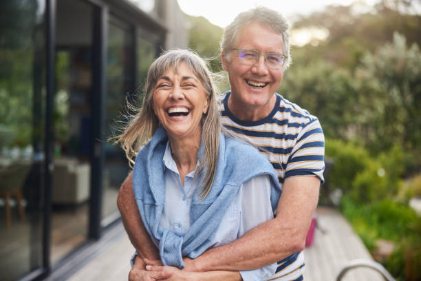 Mature couple standing arm in arm and laughing outside in summer Mature couple standing arm in arm together and laughing outside in the back yard at home in summer wife stock pictures, royalty-free photos & images