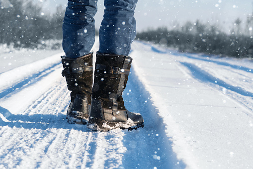 Close up of men's winter boots in snow. The man in boots walks along a snowy winter road. Sunset in the winter forest.