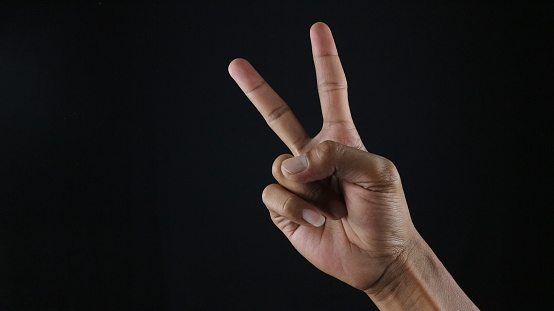 Man raising two fingers up on hand it is shows peace strength fight or victory symbol and letter V in sign language on black background.